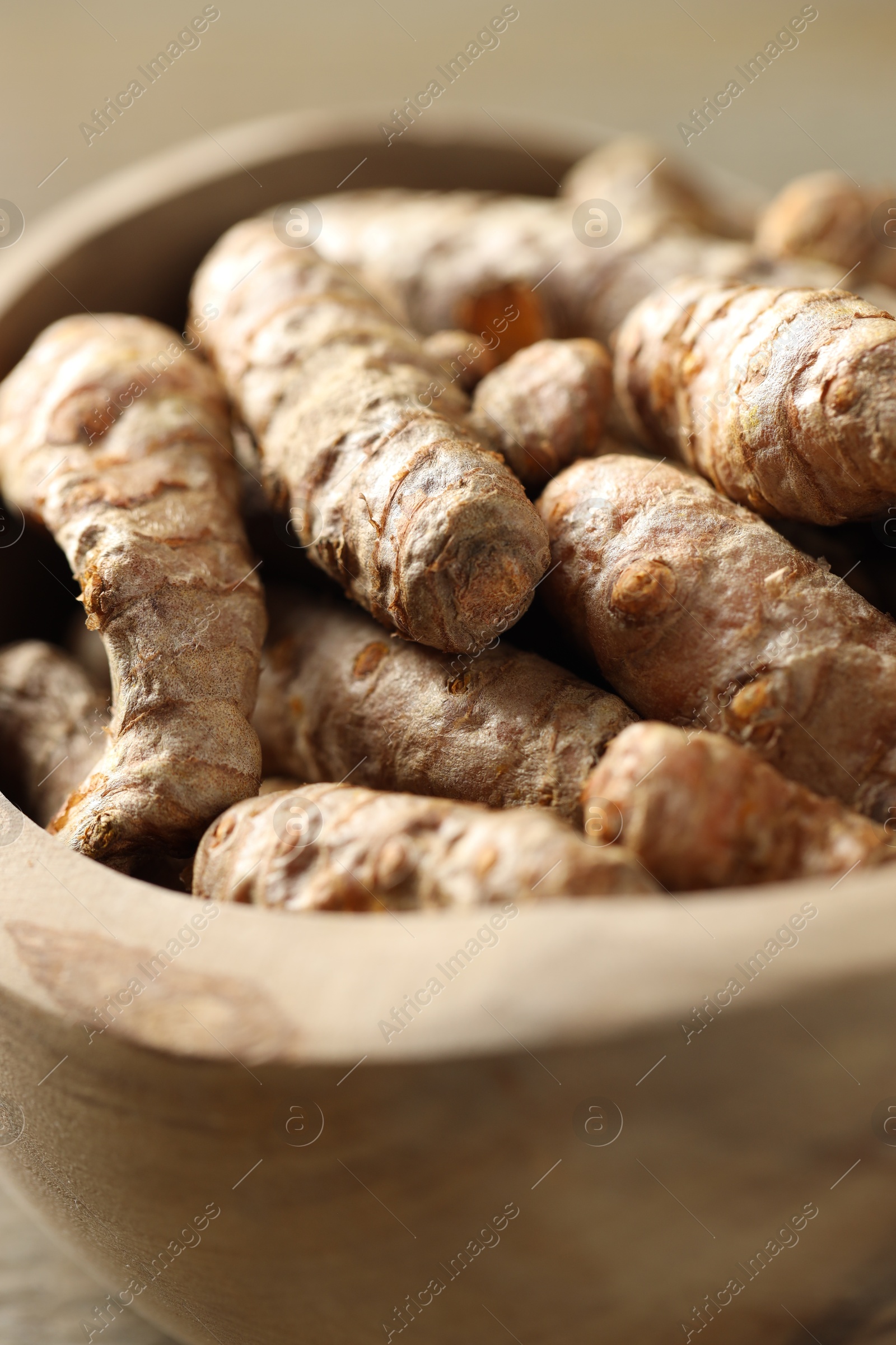 Photo of Raw turmeric roots in bowl on table, closeup