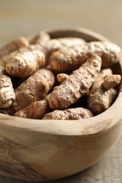 Photo of Raw turmeric roots in bowl on table, closeup