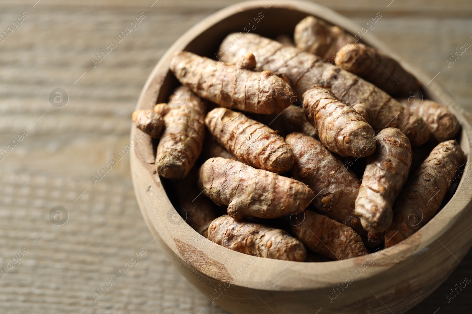 Photo of Raw turmeric roots in bowl on wooden table, closeup