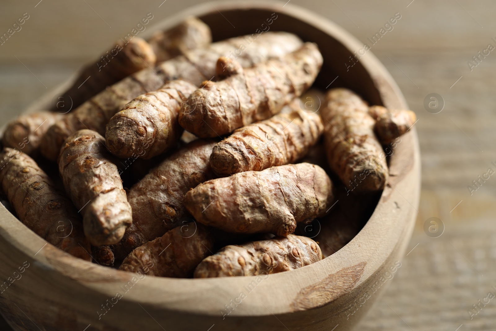 Photo of Raw turmeric roots in bowl on wooden table, closeup