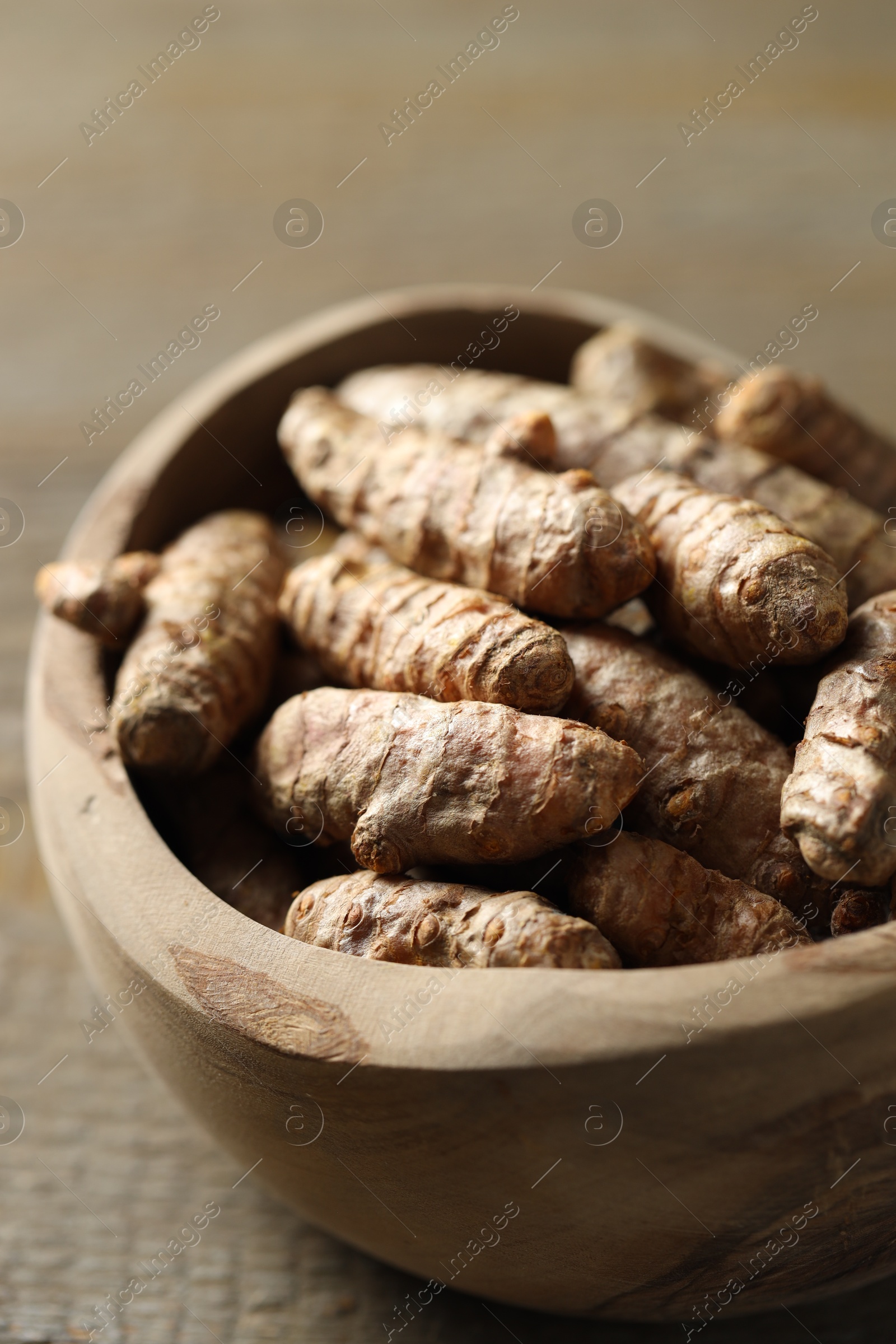 Photo of Raw turmeric roots in bowl on wooden table, closeup