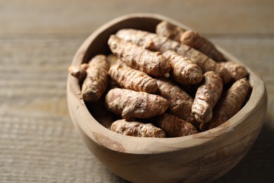 Photo of Raw turmeric roots in bowl on wooden table, closeup