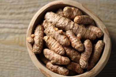 Photo of Raw turmeric roots in bowl on wooden table, closeup