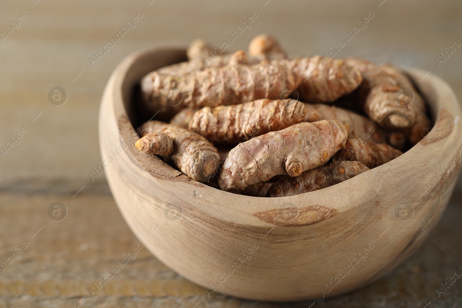 Photo of Raw turmeric roots in bowl on wooden table, closeup