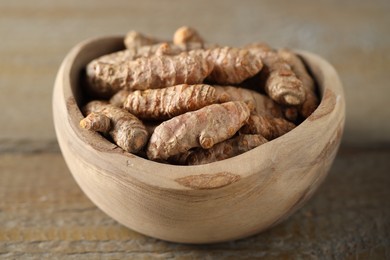 Photo of Raw turmeric roots in bowl on wooden table, closeup