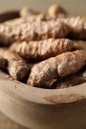 Photo of Raw turmeric roots in wooden bowl, closeup