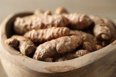 Photo of Raw turmeric roots in wooden bowl, closeup