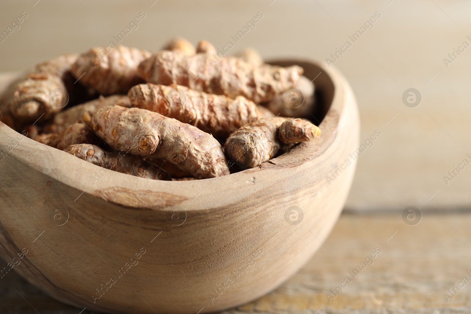 Photo of Raw turmeric roots in bowl on wooden table, closeup