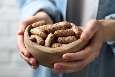 Photo of Woman holding bowl with raw turmeric roots on light background, closeup