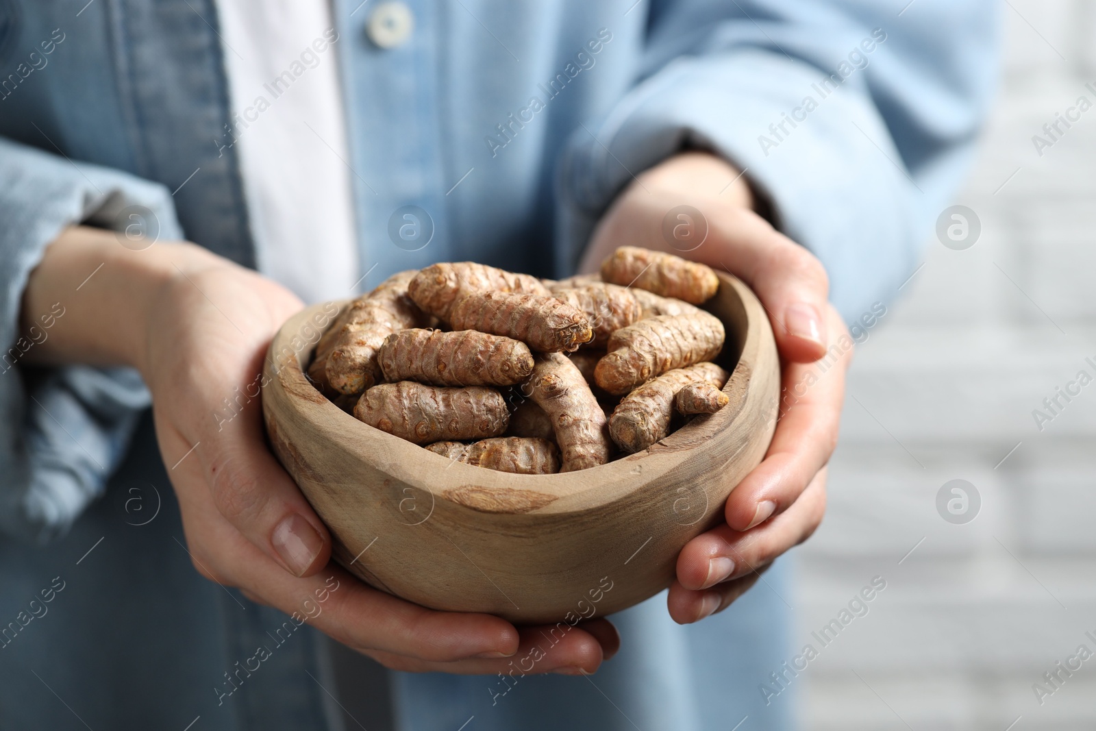 Photo of Woman holding bowl with raw turmeric roots on light background, closeup