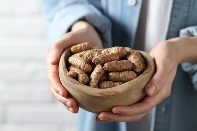 Photo of Woman holding bowl with raw turmeric roots on light background, closeup