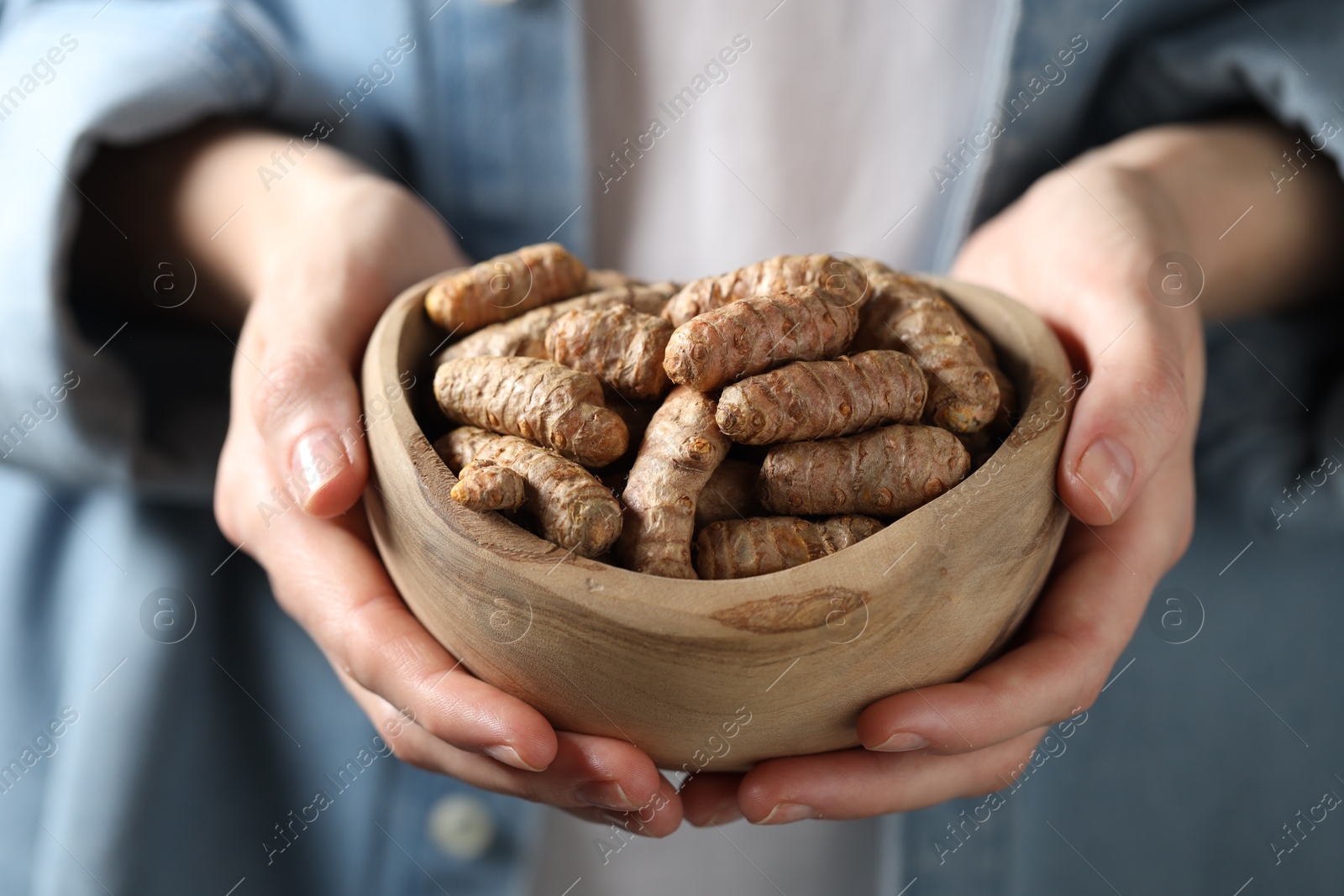 Photo of Woman holding bowl with raw turmeric roots, closeup view