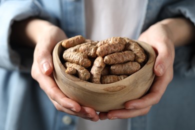 Photo of Woman holding bowl with raw turmeric roots, closeup view