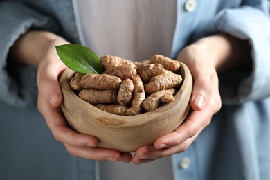 Photo of Woman holding bowl with raw turmeric roots, closeup