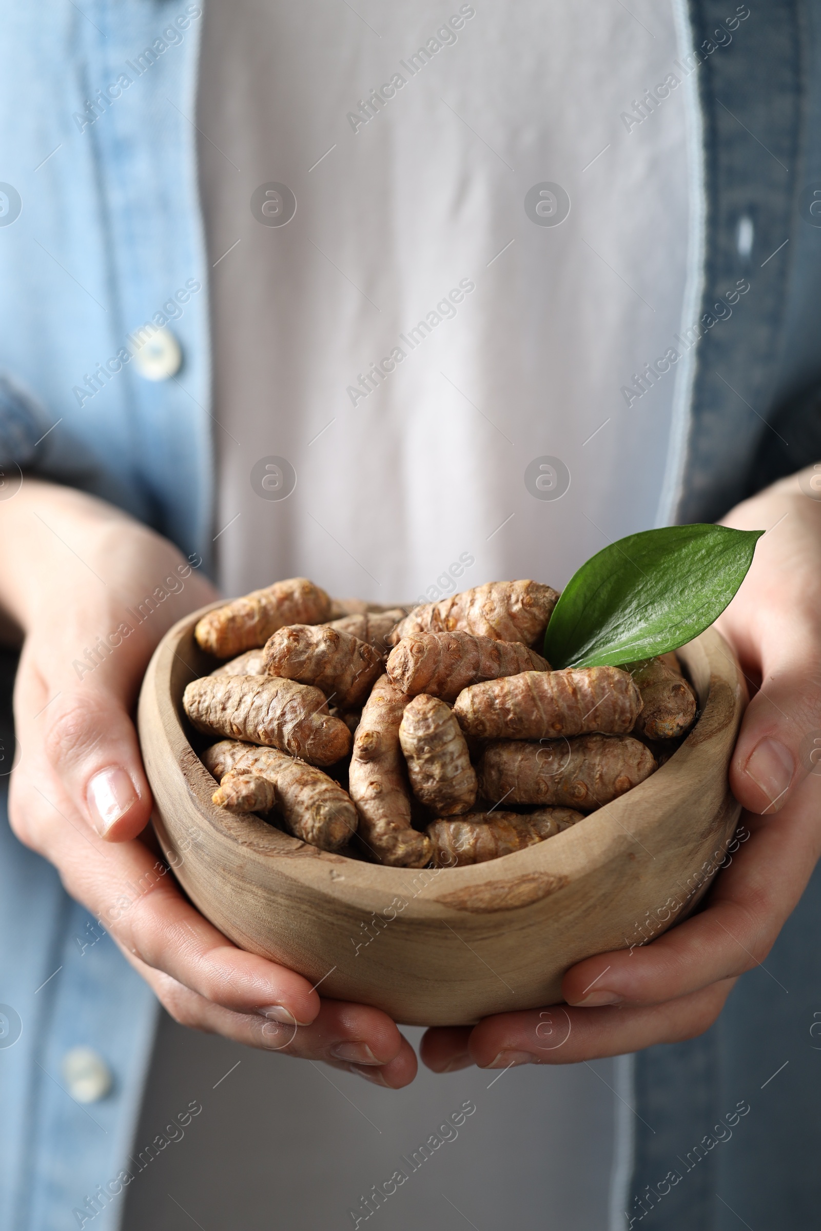 Photo of Woman holding bowl with raw turmeric roots, closeup