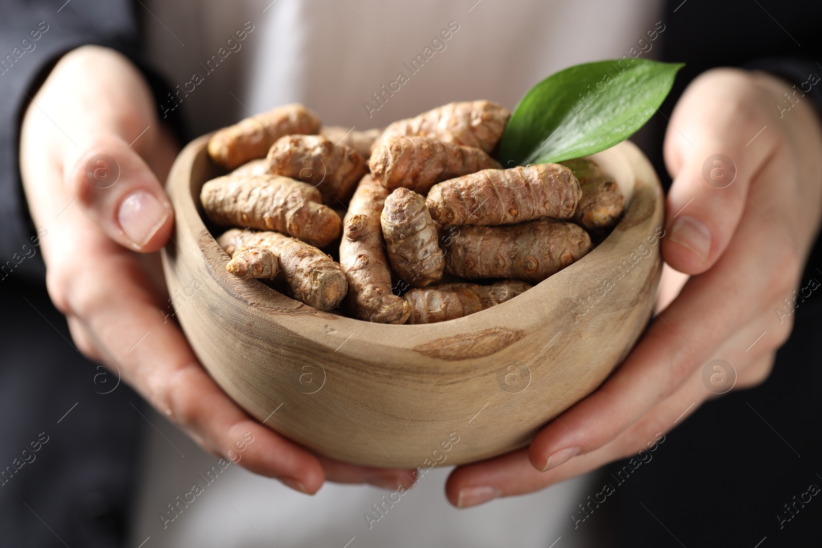 Photo of Woman holding bowl with raw turmeric roots, closeup