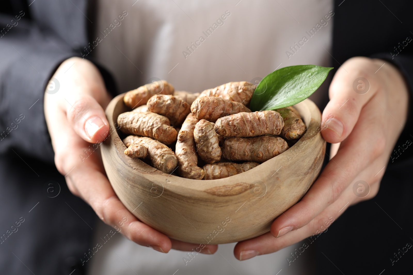 Photo of Woman holding bowl with raw turmeric roots, closeup