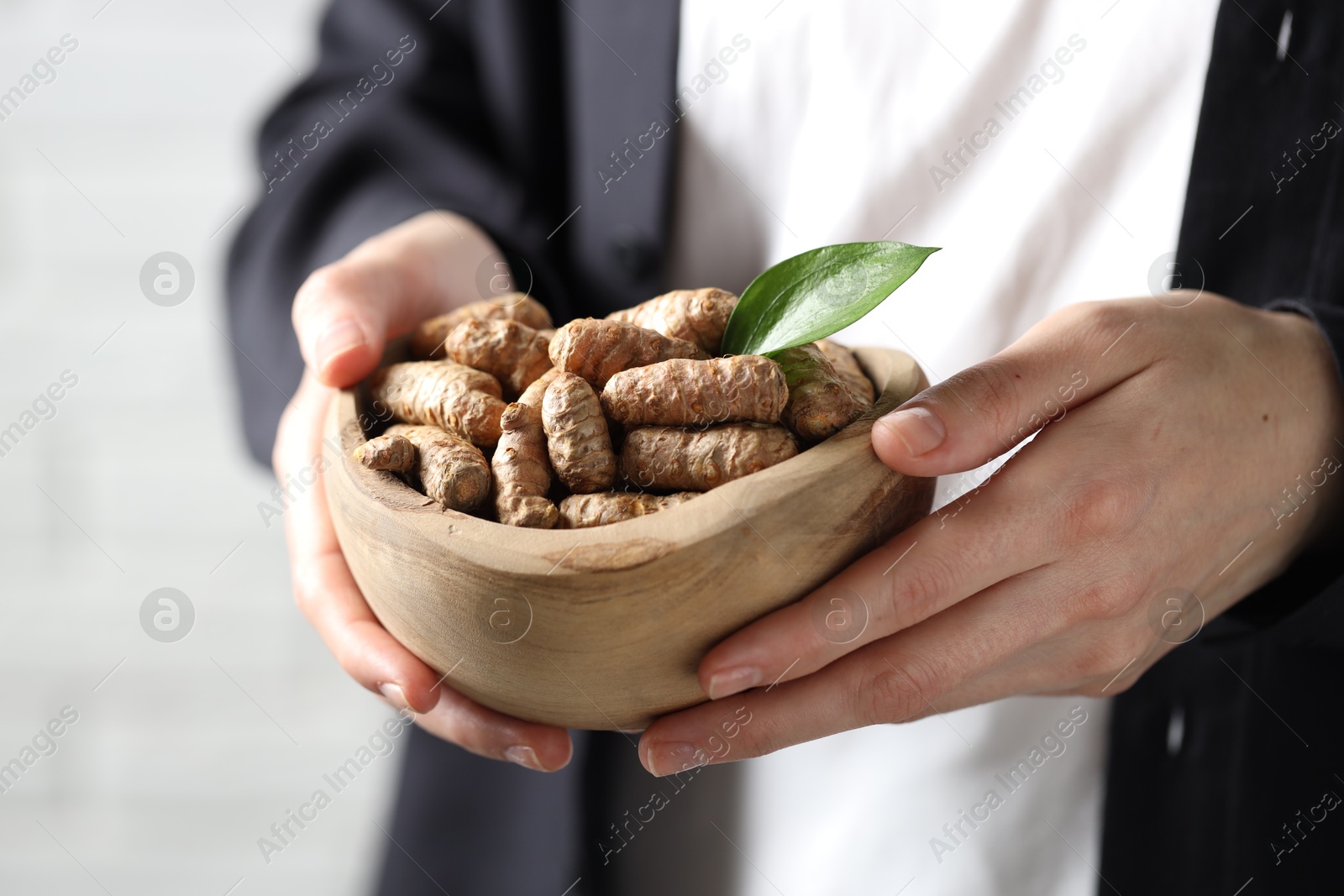 Woman holding bowl with raw turmeric roots on light background, closeup Photo of Woman holding bowl with raw turmeric roots on light background, closeup