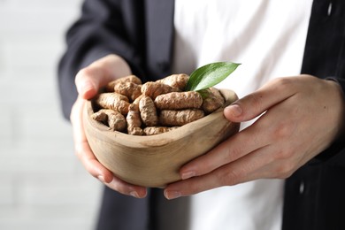 Photo of Woman holding bowl with raw turmeric roots on light background, closeup