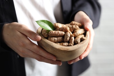 Photo of Woman holding bowl with raw turmeric roots on light background, closeup