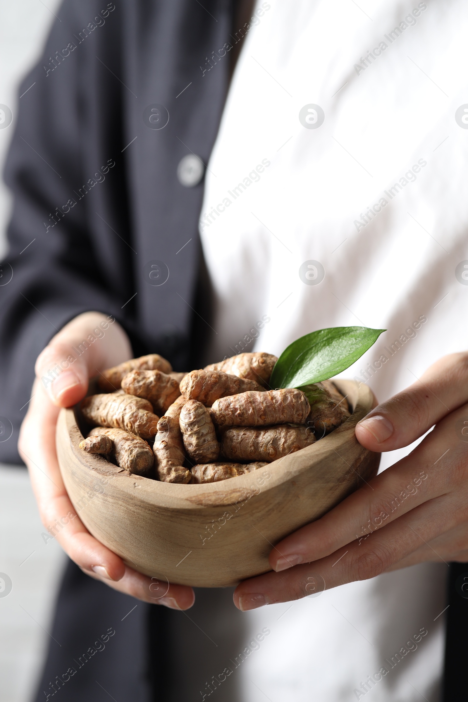 Photo of Woman holding bowl with raw turmeric roots, closeup