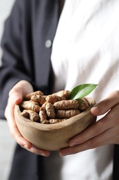 Photo of Woman holding bowl with raw turmeric roots, closeup