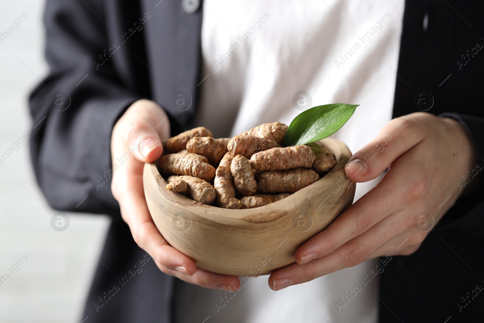 Photo of Woman holding bowl with raw turmeric roots on light background, closeup