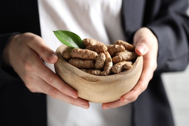 Photo of Woman holding bowl with raw turmeric roots on light background, closeup