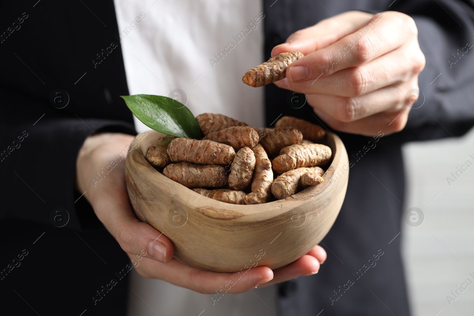 Photo of Woman holding bowl with raw turmeric roots, closeup