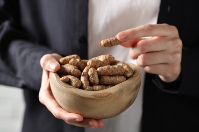 Photo of Woman holding bowl with raw turmeric roots, closeup