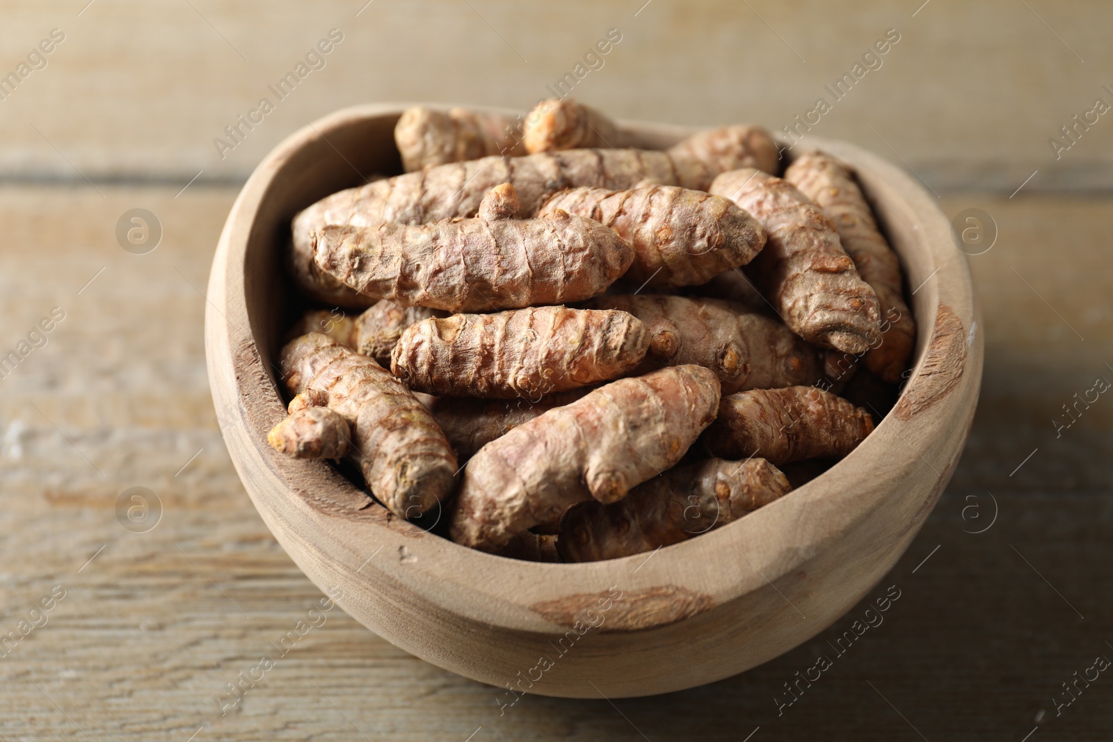 Photo of Raw turmeric roots in bowl on wooden table, closeup