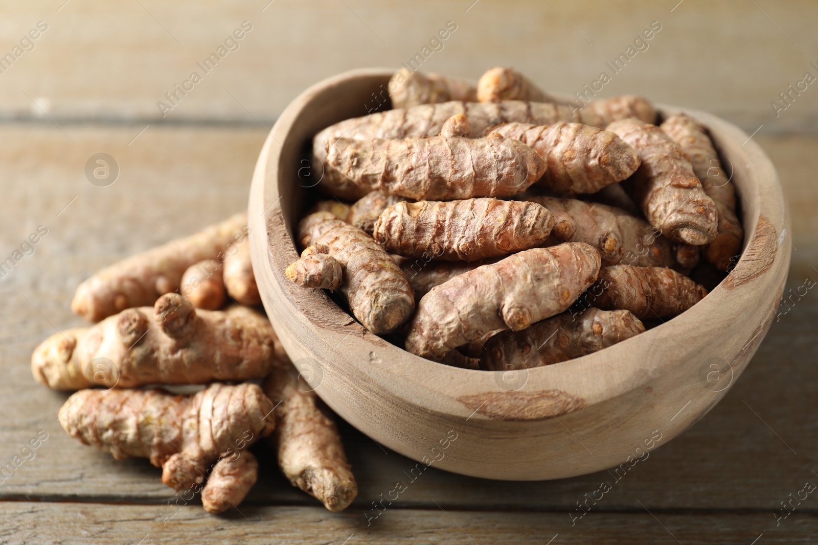 Photo of Raw turmeric roots in bowl on wooden table, closeup