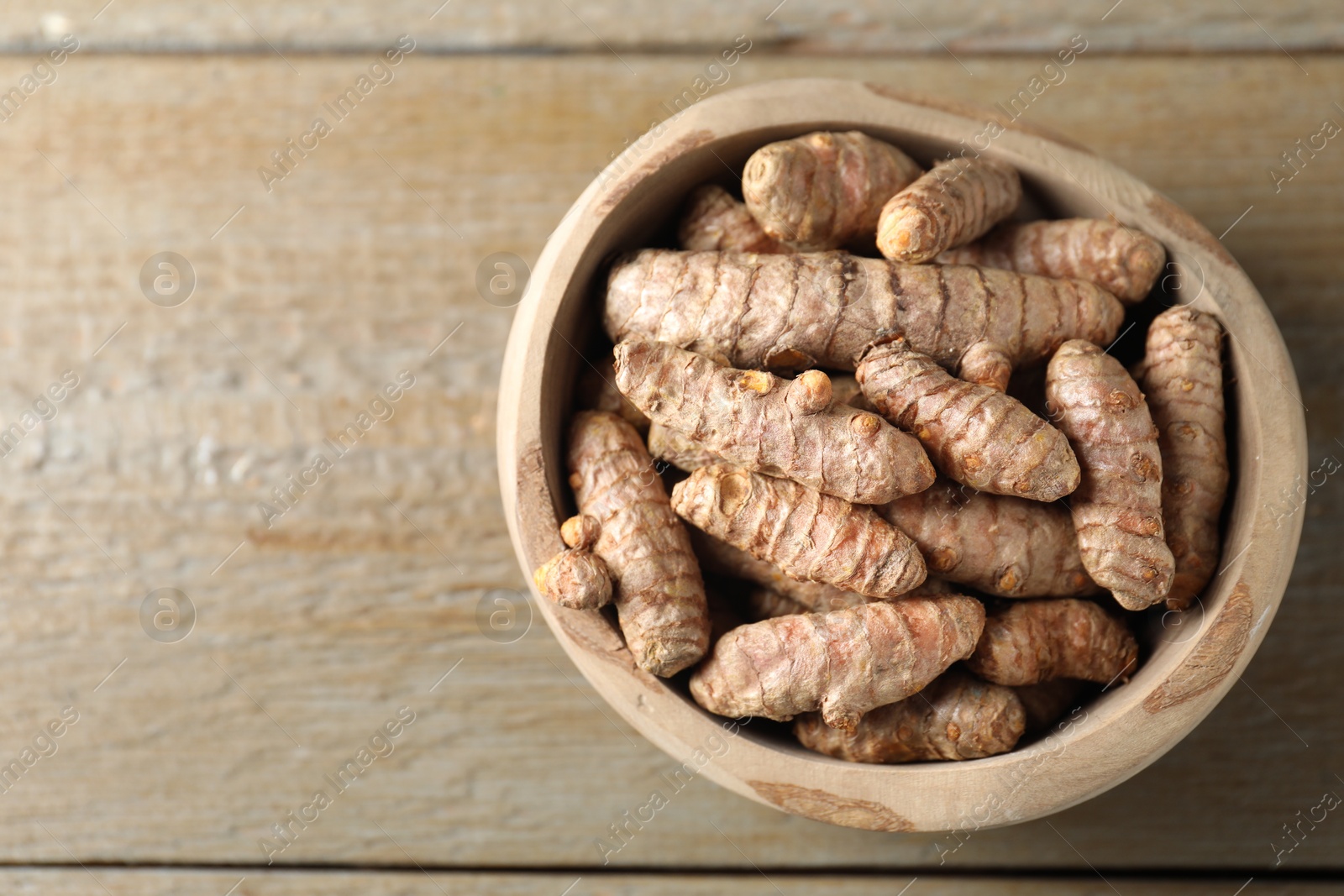 Photo of Raw turmeric roots in bowl on wooden table, top view. Space for text