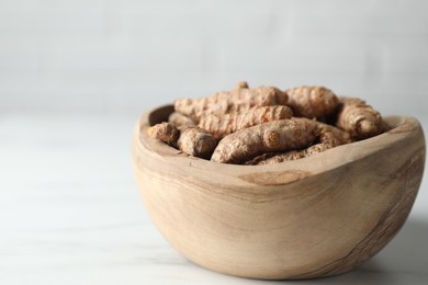 Photo of Raw turmeric roots in bowl on white table, closeup. Space for text