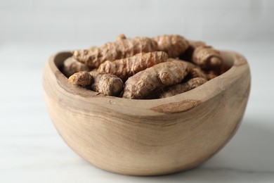 Photo of Raw turmeric roots in bowl on white marble table, closeup