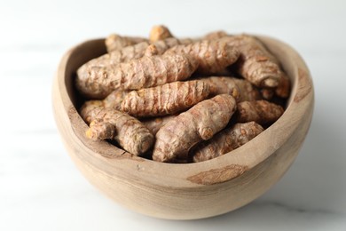 Photo of Raw turmeric roots in bowl on white marble table, closeup