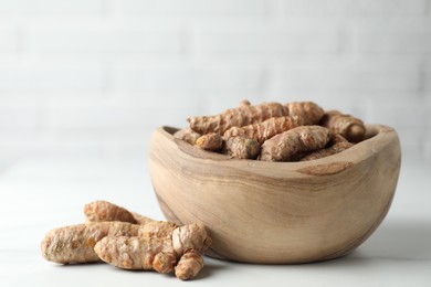 Photo of Raw turmeric roots in bowl on white table, closeup