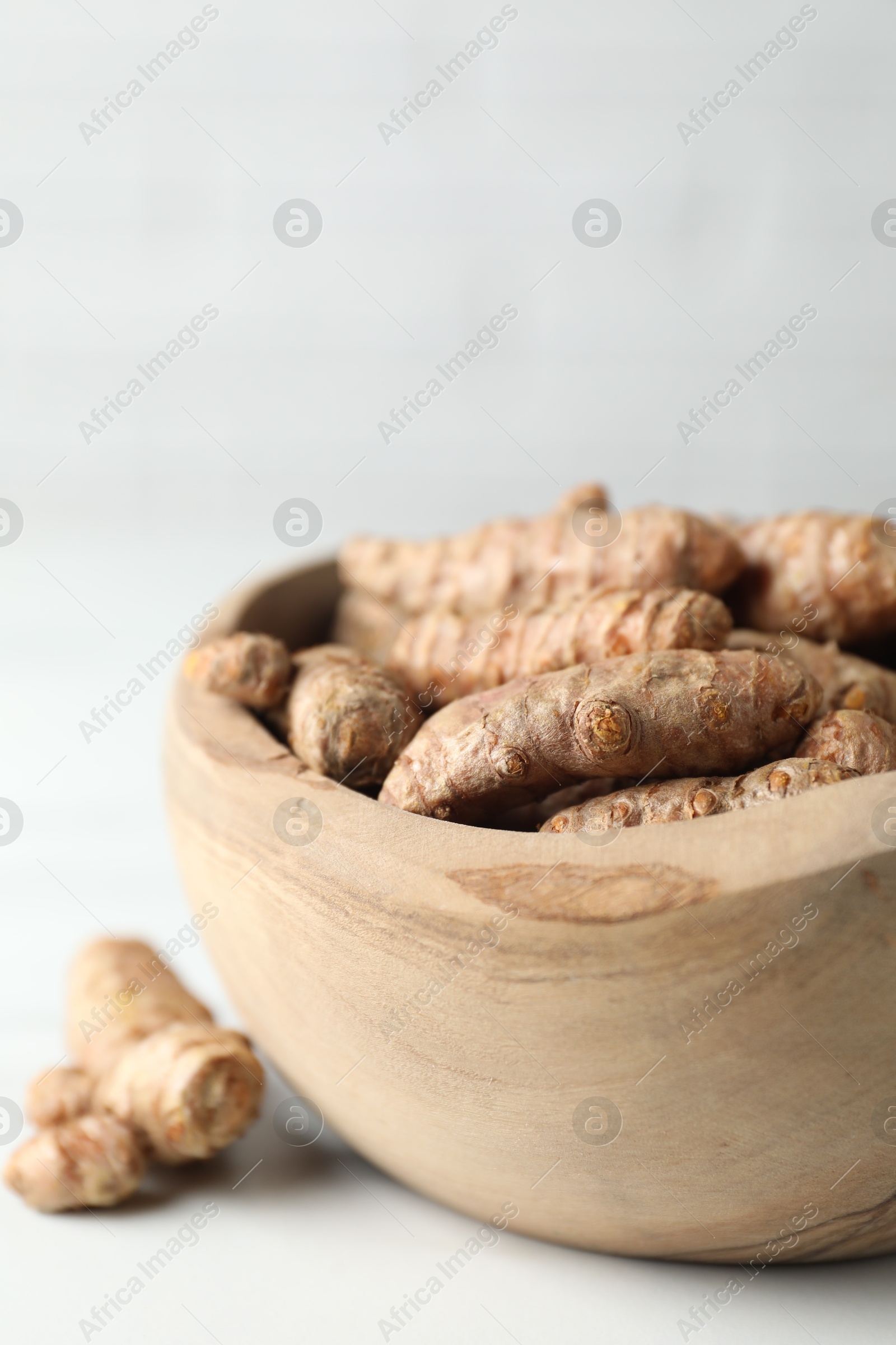 Photo of Raw turmeric roots in bowl on white table, closeup