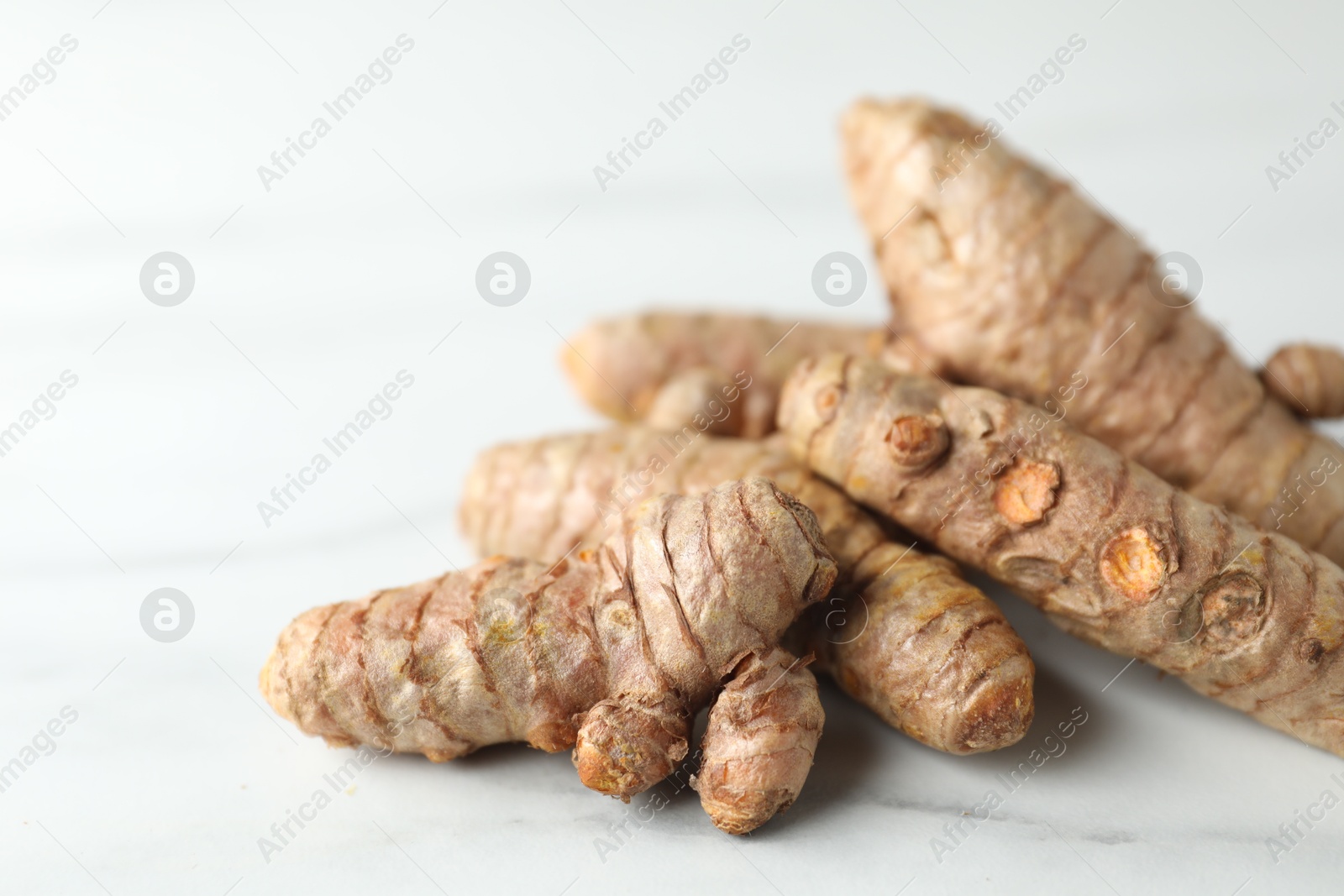 Photo of Pile of raw turmeric roots on white marble table, closeup. Space for text