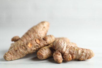 Photo of Raw turmeric roots on white marble table, closeup