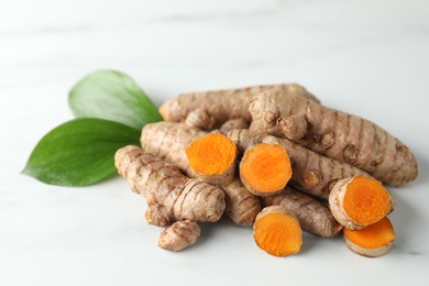 Photo of Raw turmeric roots and green leaves on white marble table, closeup