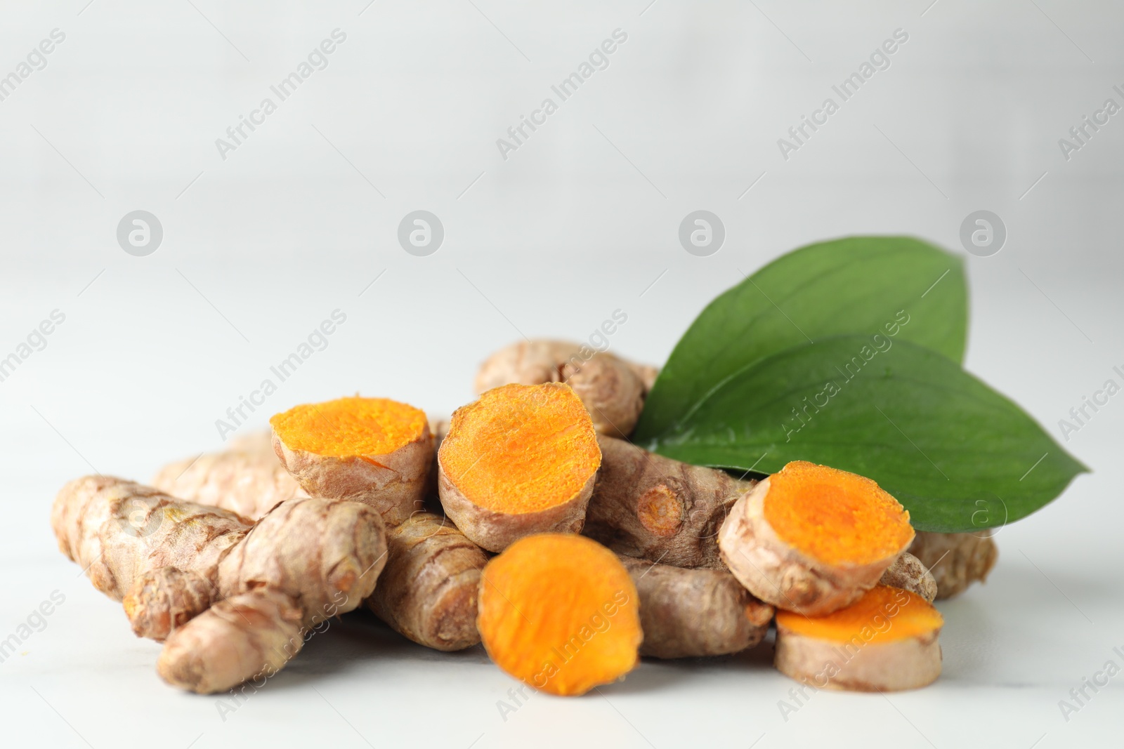 Photo of Raw turmeric roots and green leaves on white table, closeup