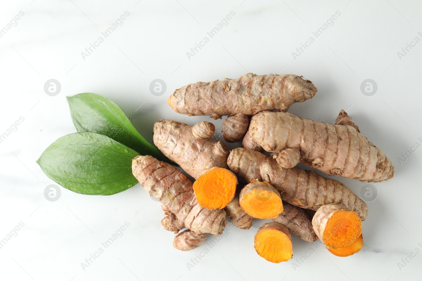 Photo of Raw turmeric roots and leaves on white marble table, flat lay