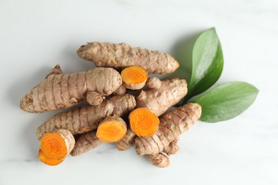 Photo of Raw turmeric roots and leaves on white marble table, flat lay