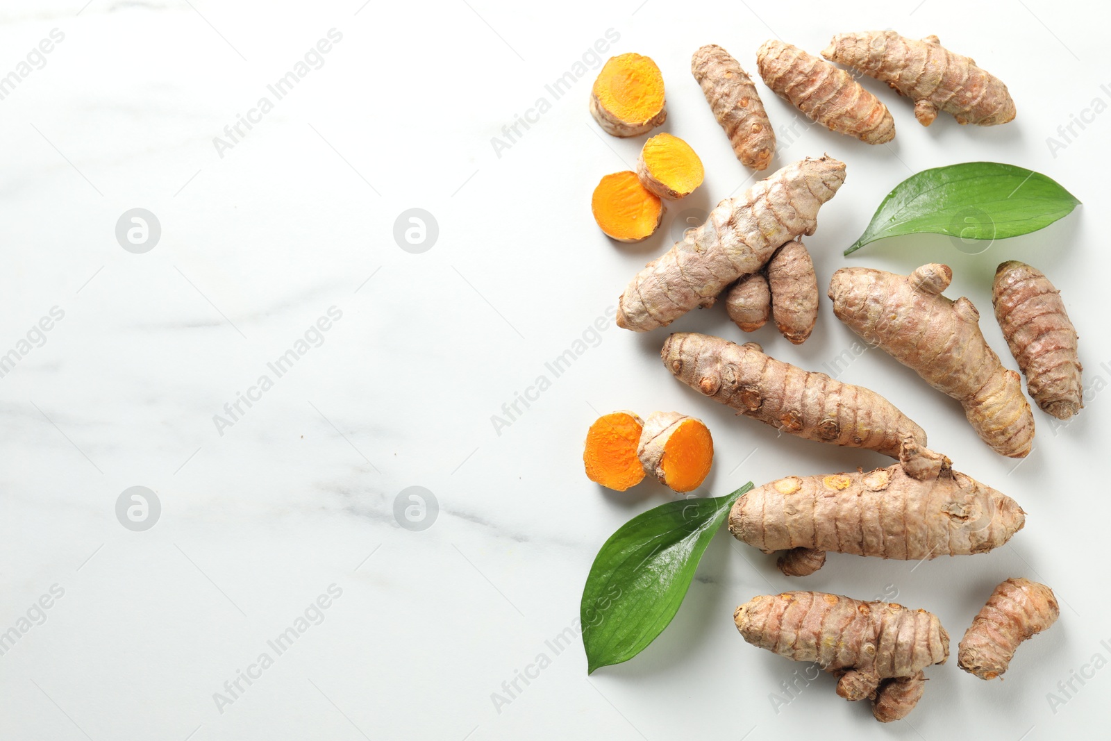 Photo of Raw turmeric roots and leaves on white marble table, flat lay. Space for text