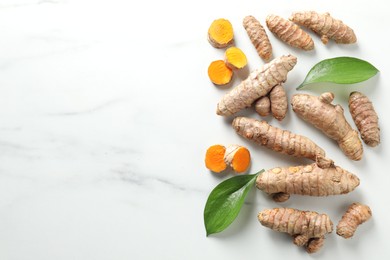 Photo of Raw turmeric roots and leaves on white marble table, flat lay. Space for text