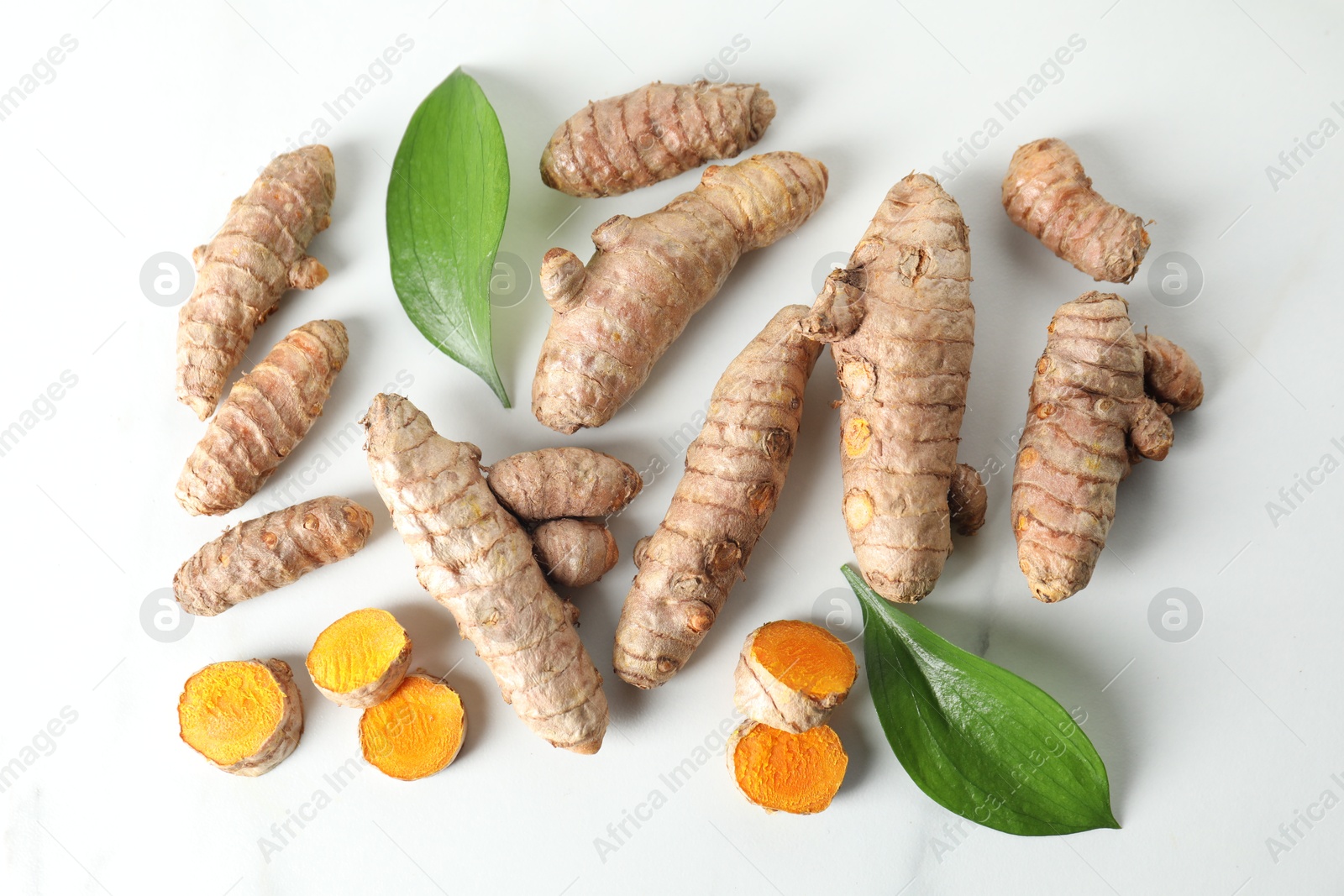 Photo of Raw turmeric roots and leaves on white marble table, flat lay