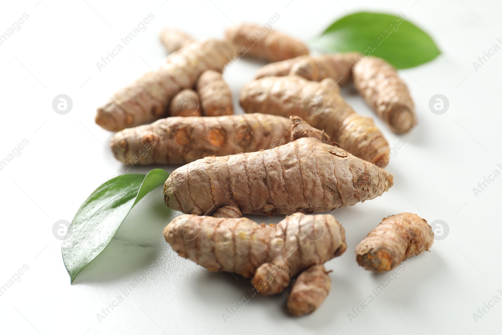 Photo of Raw turmeric roots and green leaves on white table, closeup