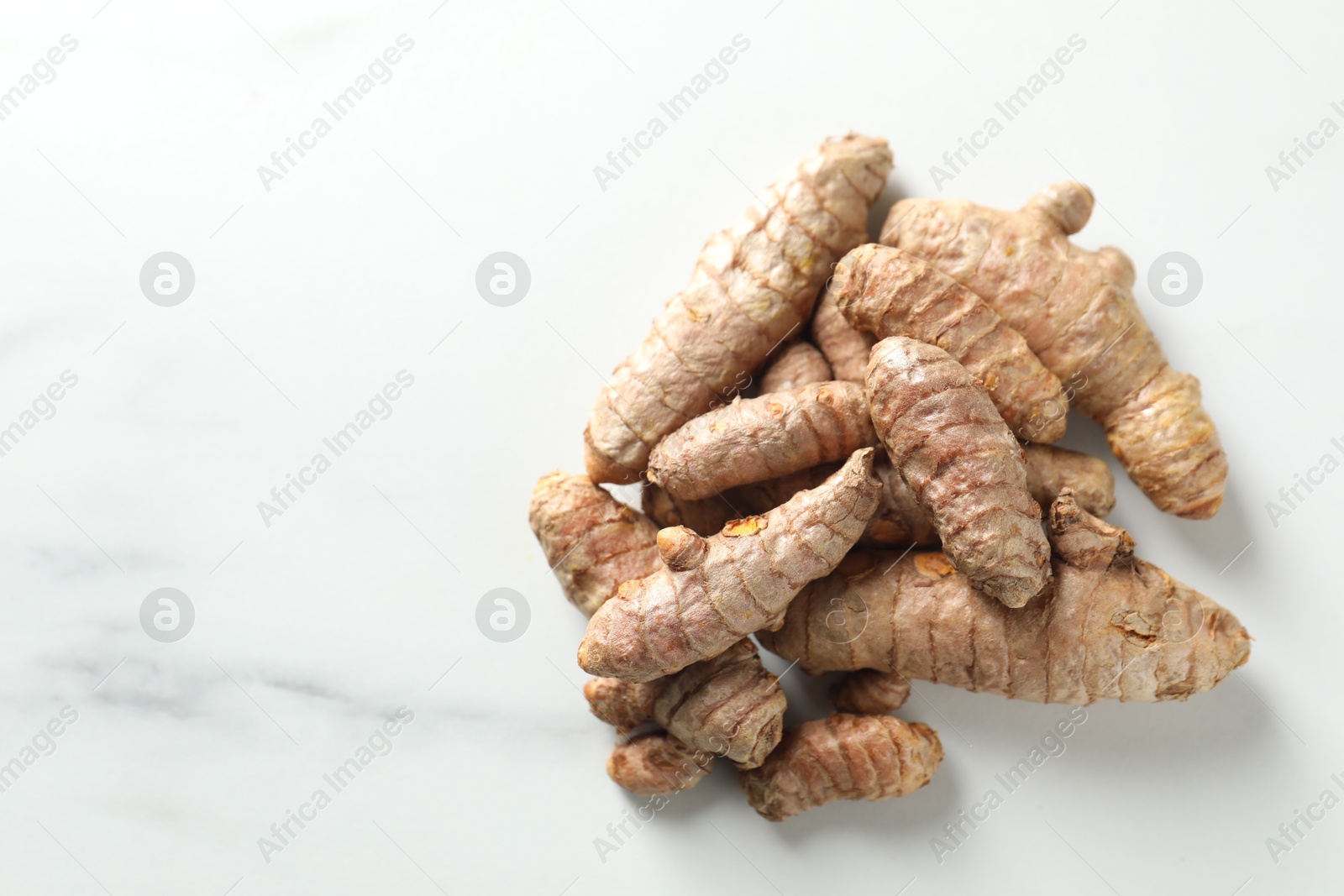 Photo of Pile of raw turmeric roots on white marble table, top view. Space for text