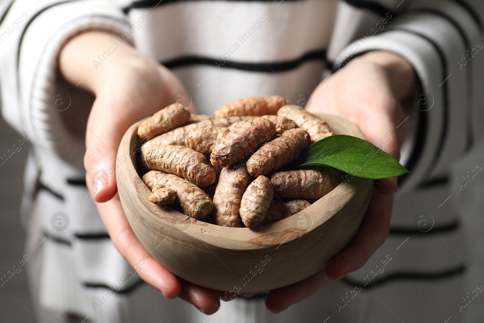 Photo of Woman holding bowl with raw turmeric roots, closeup